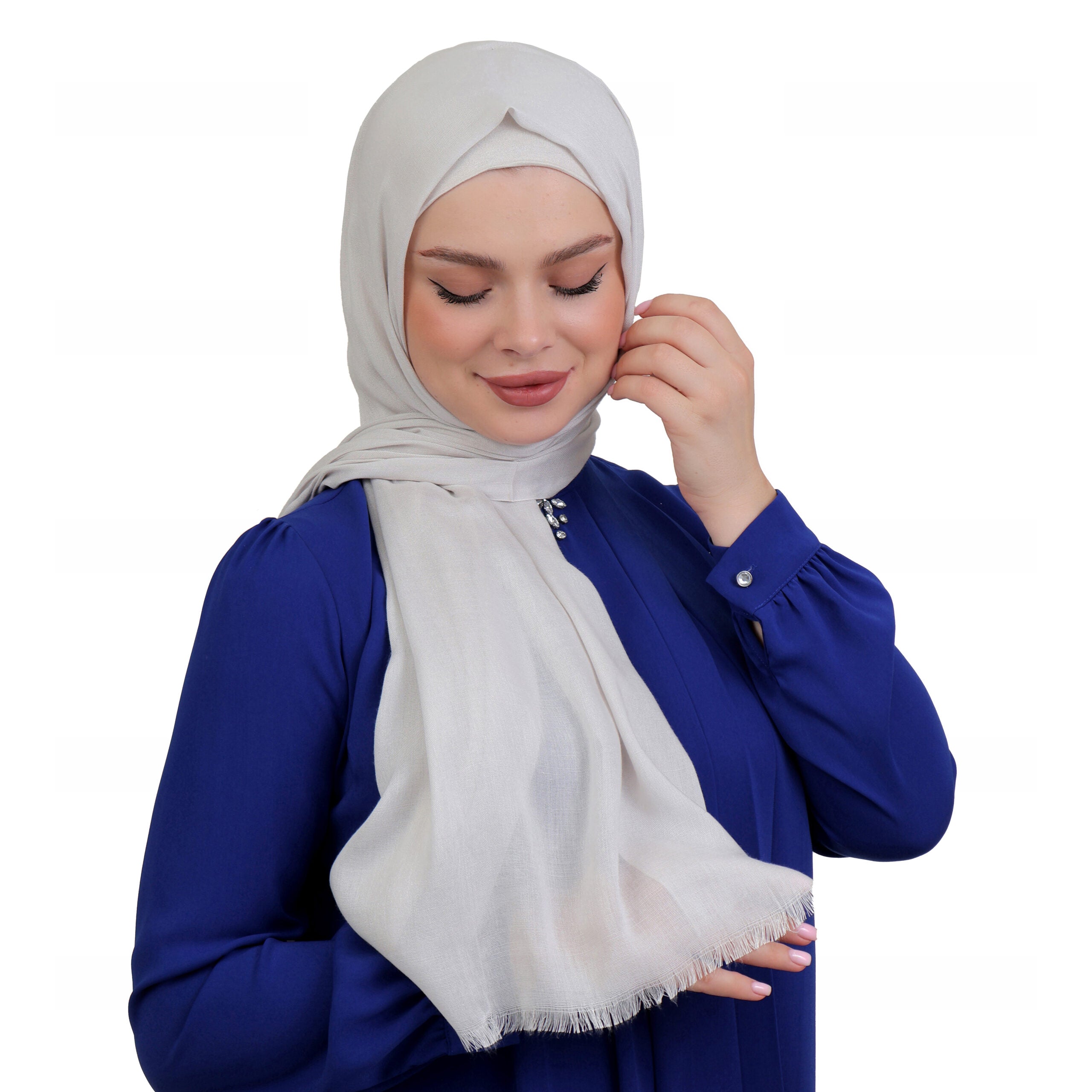 Model elegantly adjusting an off-white hijab, styled with a sleek royal blue top for a formal look.
