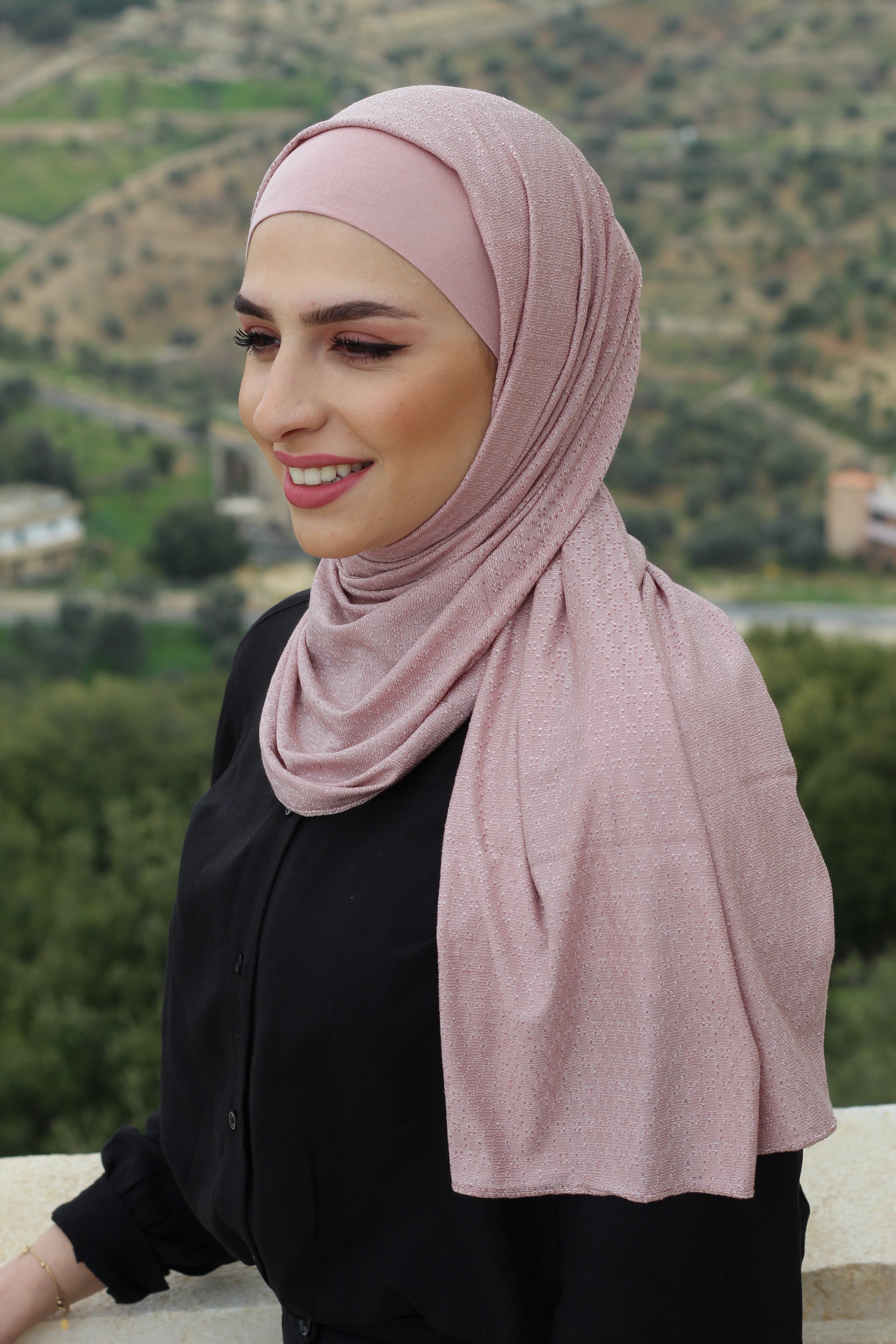Model wearing a soft pink hijab, styled casually against a picturesque outdoor backdrop