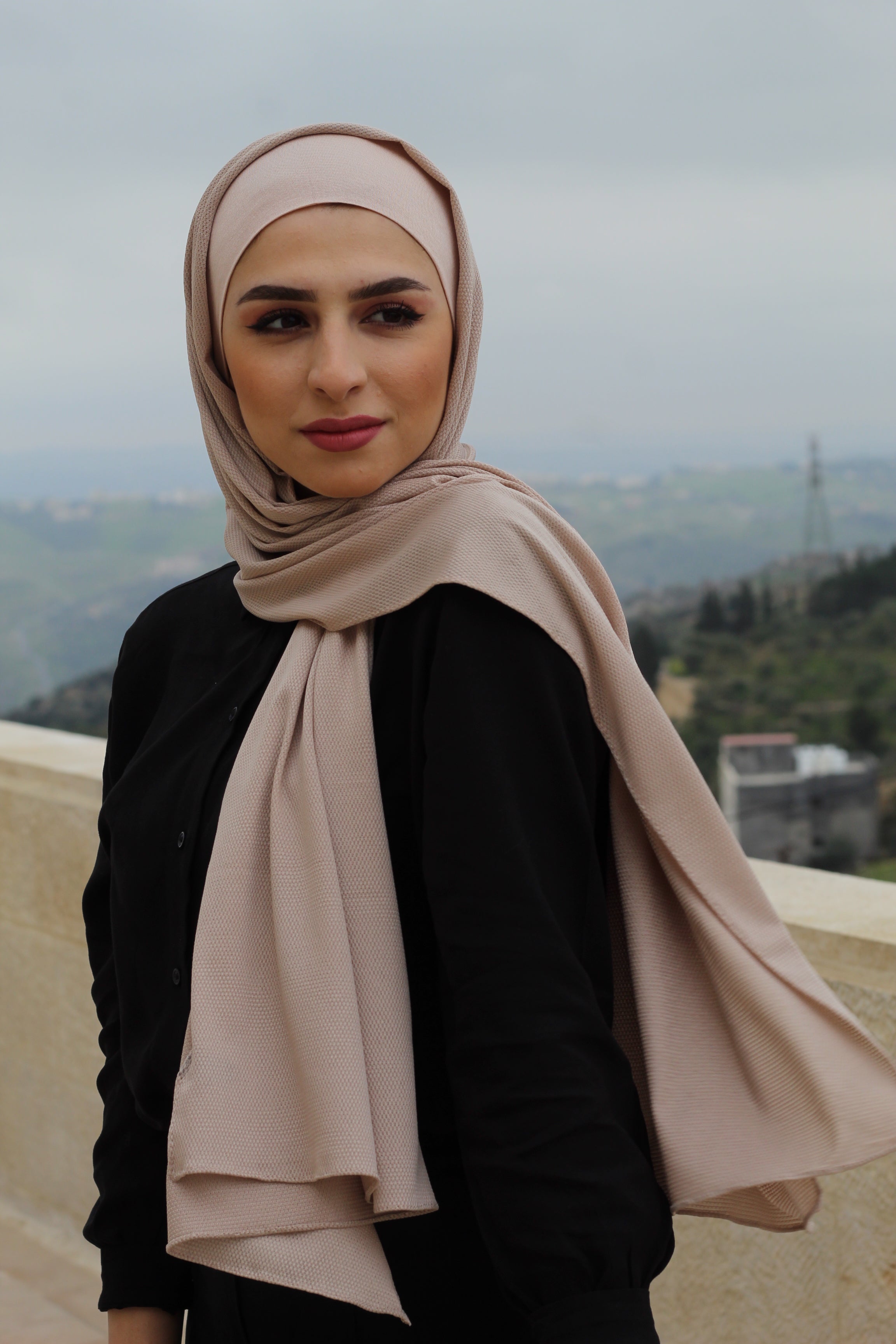 Outdoor image of a model draped in a soft blush-colored hijab, perfect for layering in colder seasons.