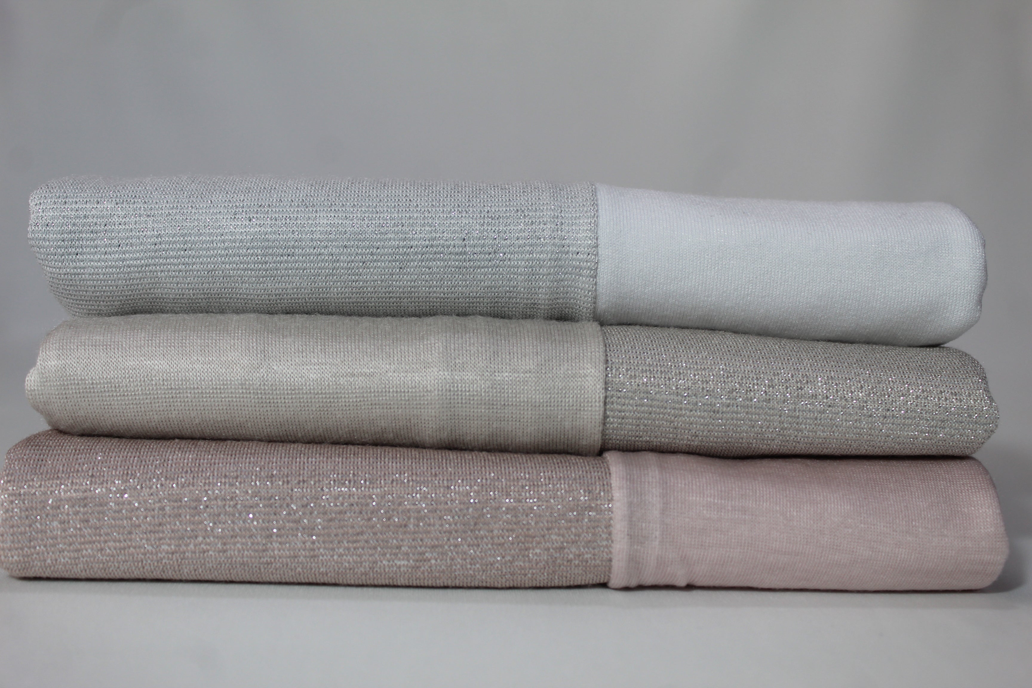 Folded hijabs in shades of grey, white, and beige, stacked to highlight their smooth texture