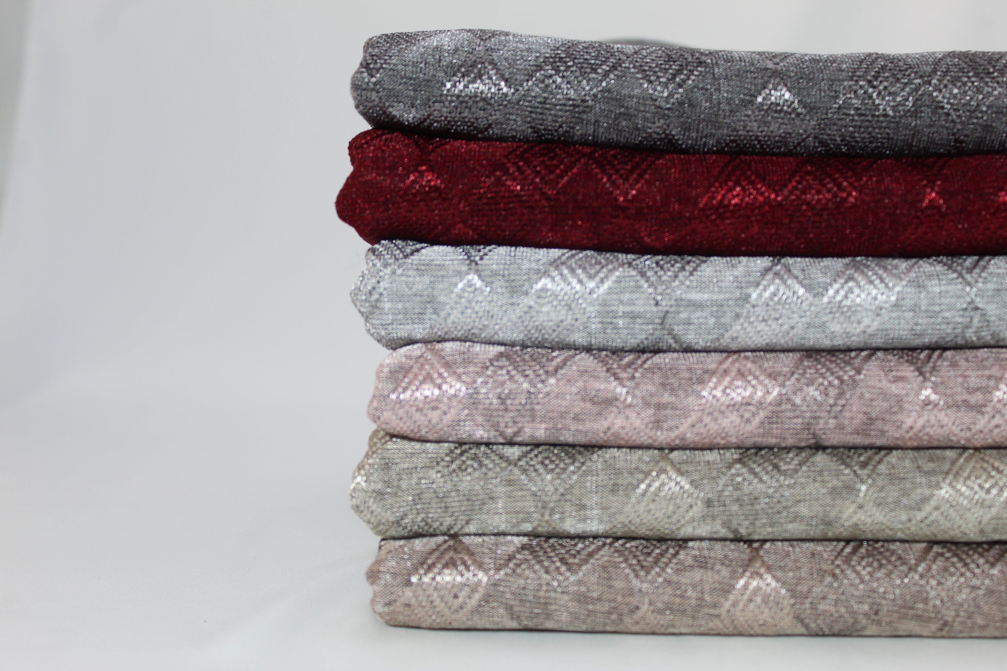 Side view of a stack of folded hijab fabrics in colors like gray, red, blue, pink, and beige, showing texture and pattern details.