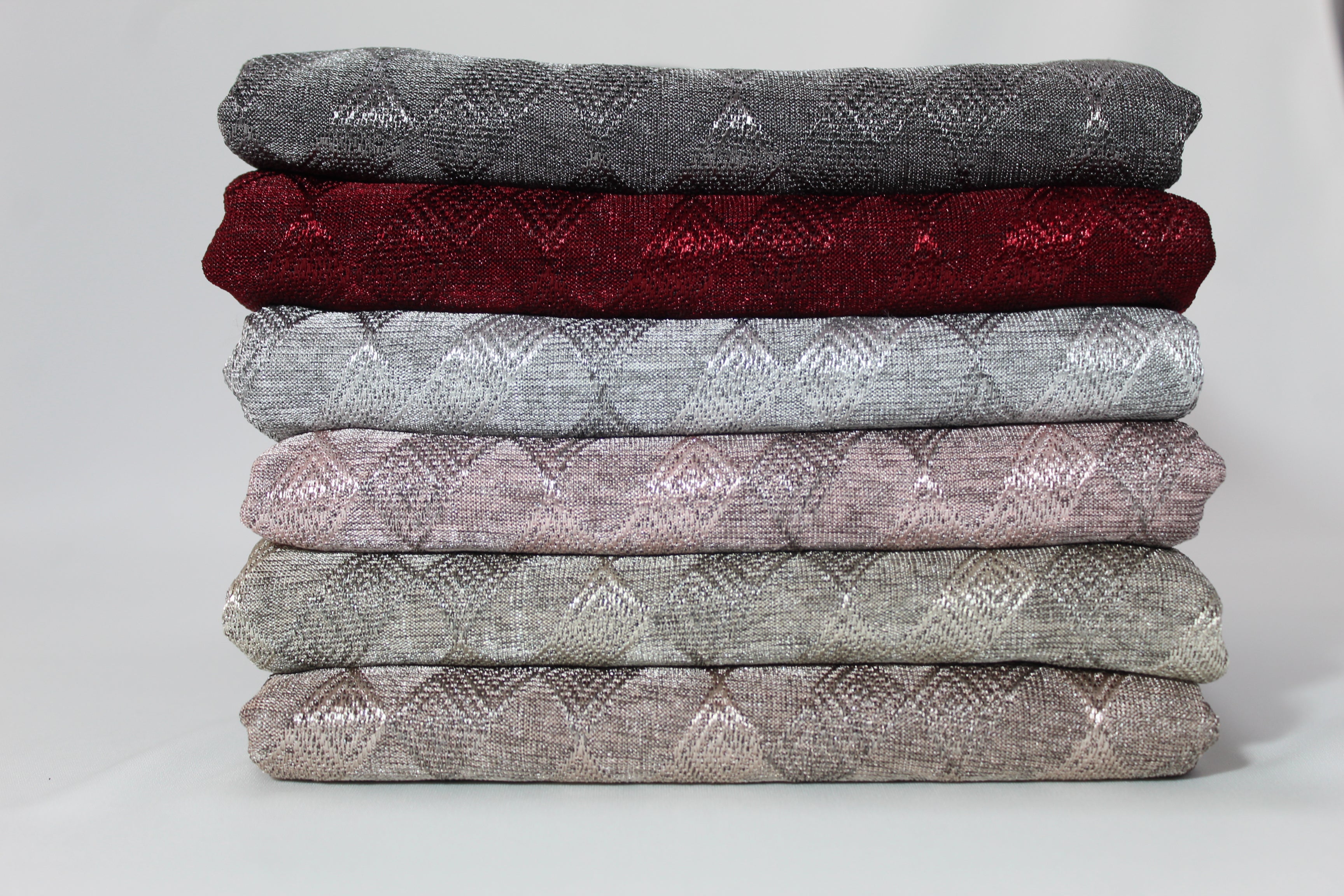 A stack of hijab fabrics in various colors, including gray, red, blue, pink, and beige, neatly folded and displayed.
