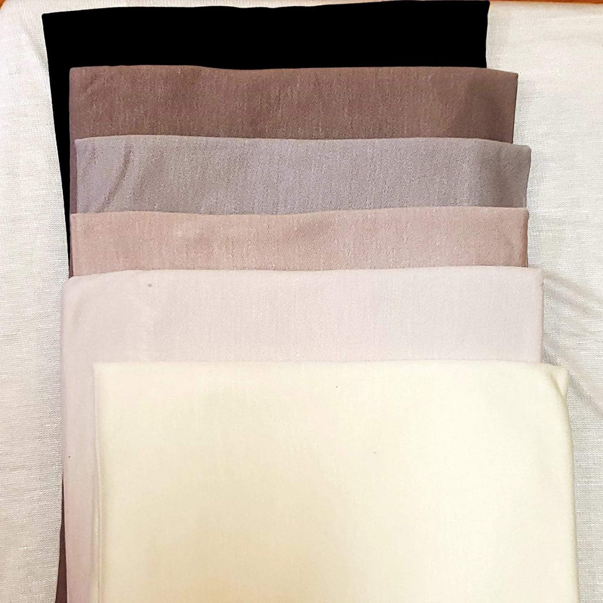 A variety of premium hijab fabrics in neutral tones, from beige to brown, folded for easy selection.