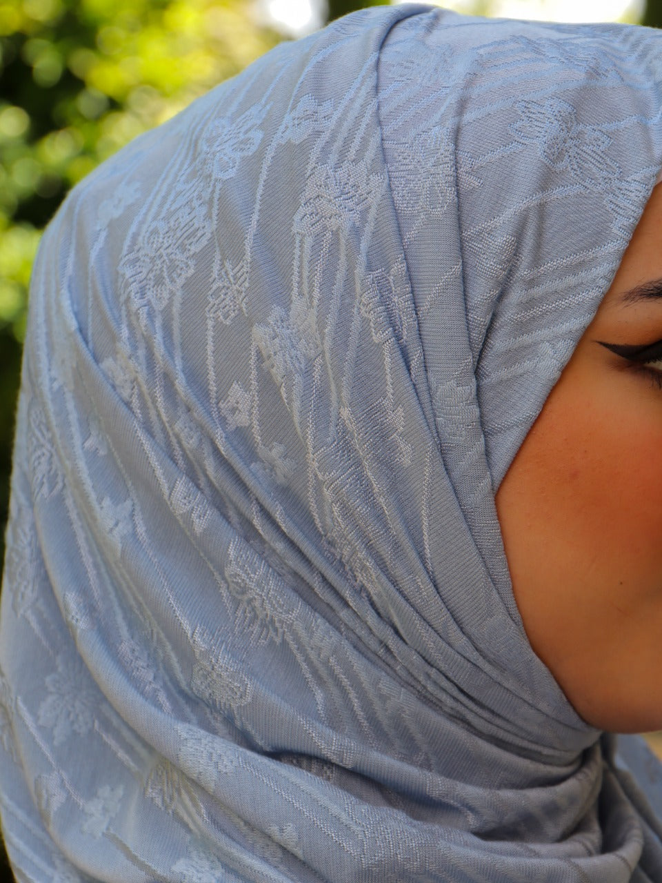 Close-up of a woman wearing a light blue hijab with delicate white patterns.