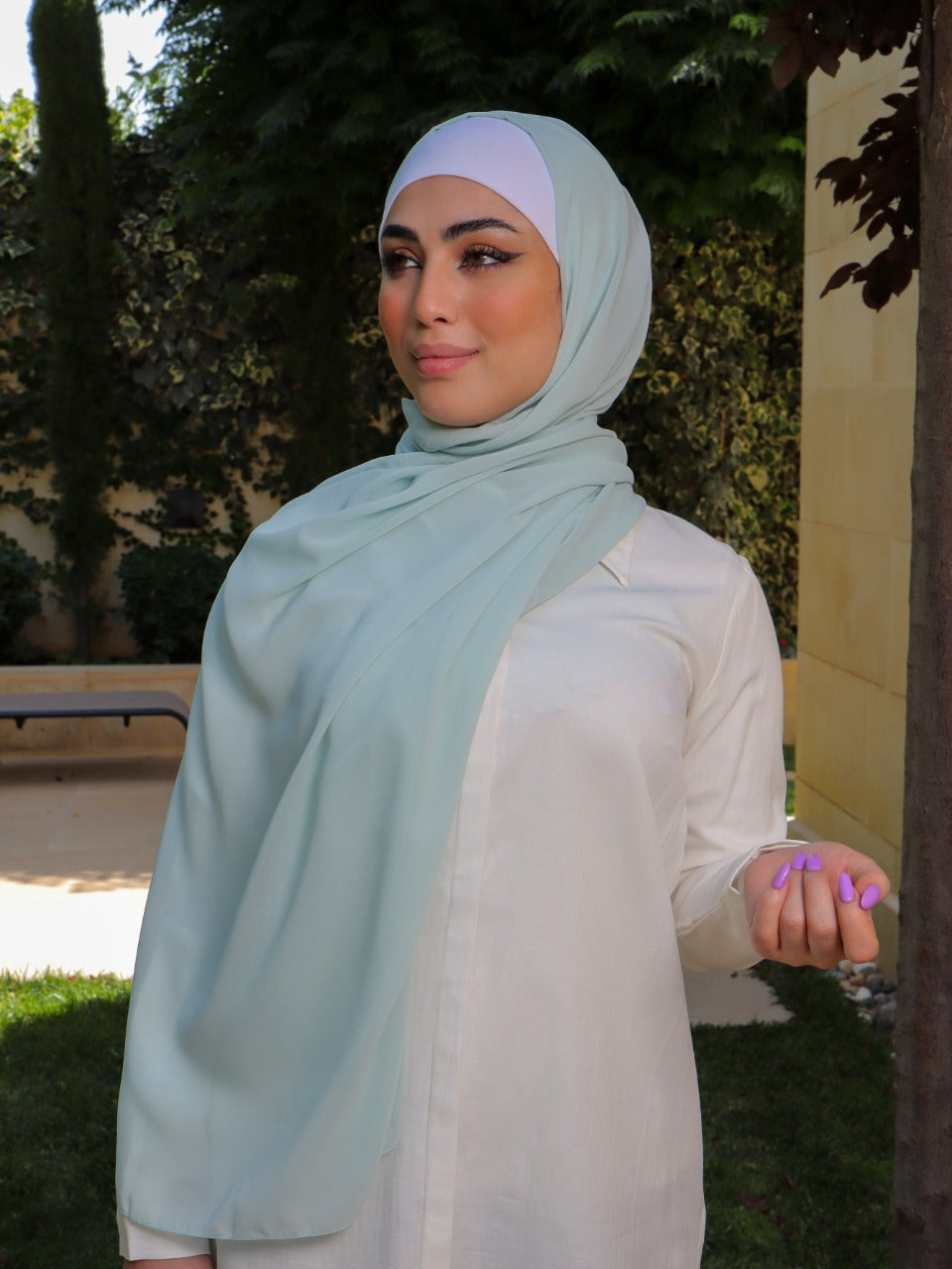 Model wearing a soft chiffon pastel blue hijab in a garden setting with elegant draping