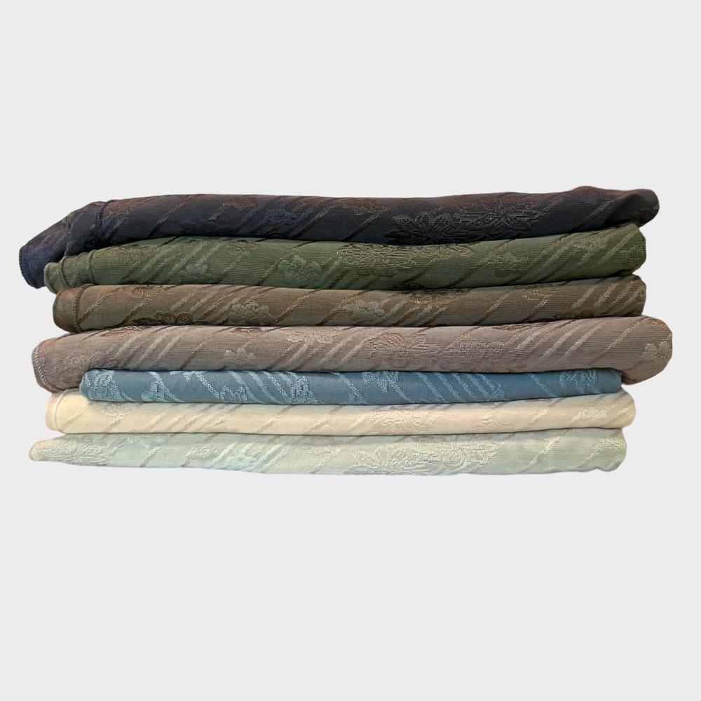 Stack of folded hijabs in various shades, including black, green, blue, and beige, displayed against a white background.
