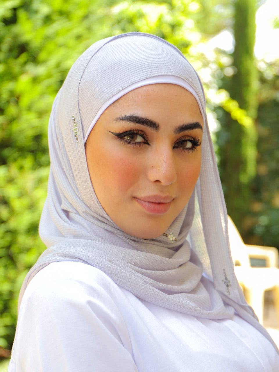 Outdoor close-up of a model wearing an ivory hijab, paired with natural makeup and a serene background.